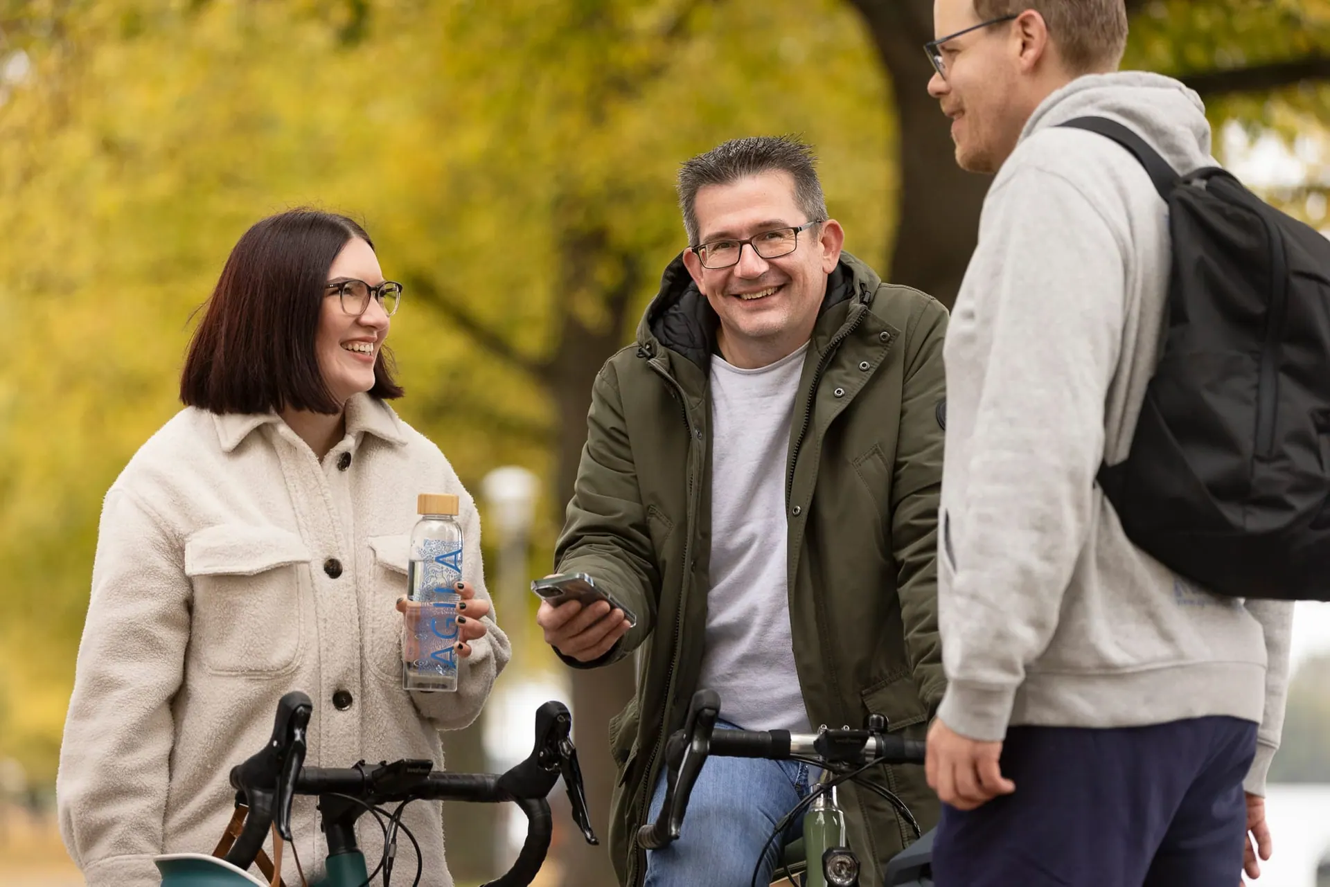 Drei Mitarbeitende mit Fahrrad vor dem Bürogebäude im Herbst