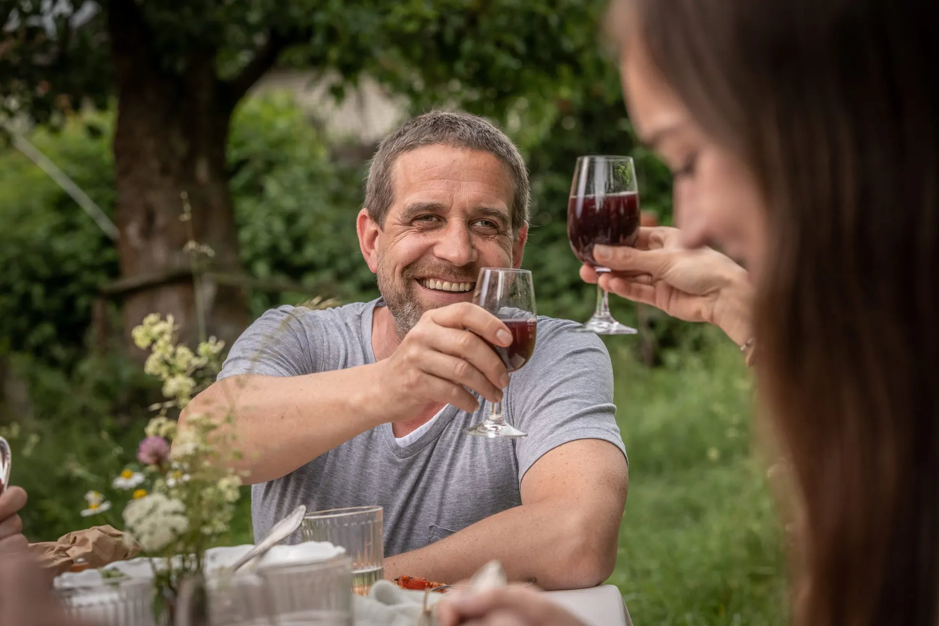 Zwei Personen stoßen mit Rotwein an einer Gartentafel an
