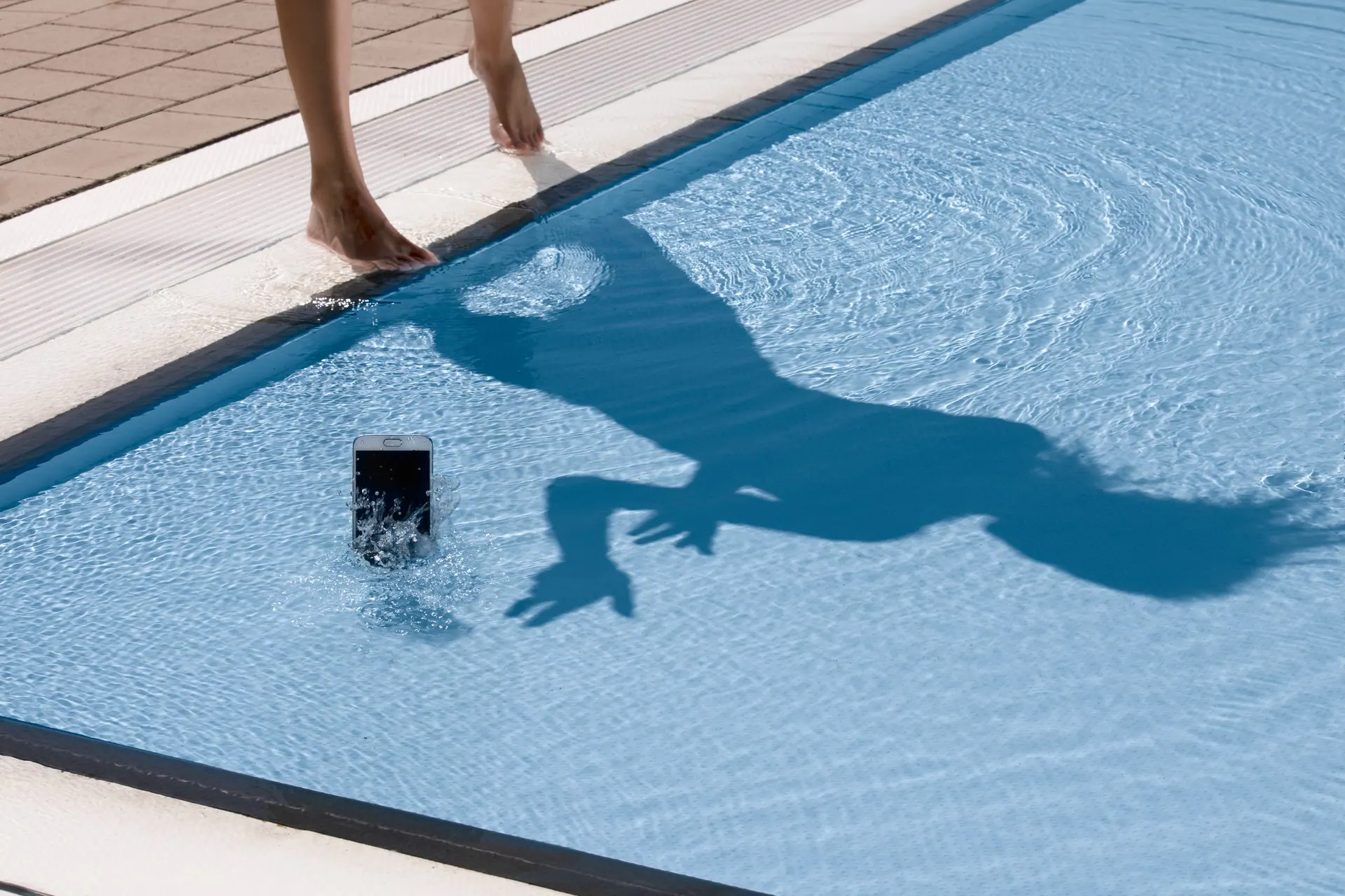 Smartphone am Grund eines Schwimmbeckens, darüber der Schatten eines Schwimmers