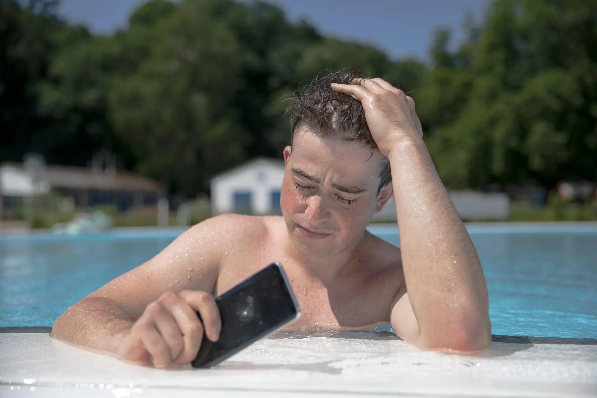 Mann im Freibad hält ein nasses Smartphone am Beckenrand