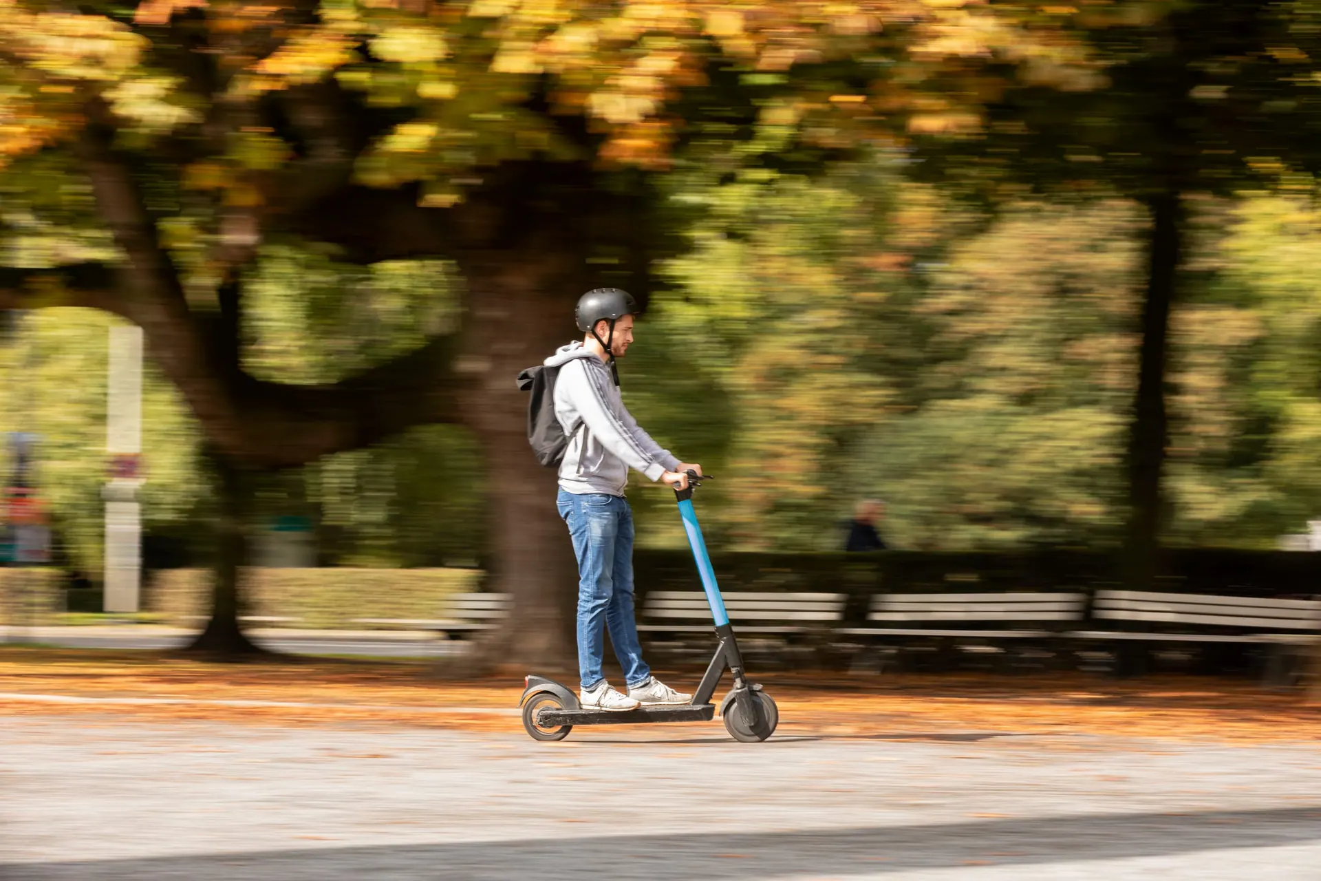 Mitgezogene Aufnahme: Person fährt auf einem E-Scooter durch eine Herbstallee