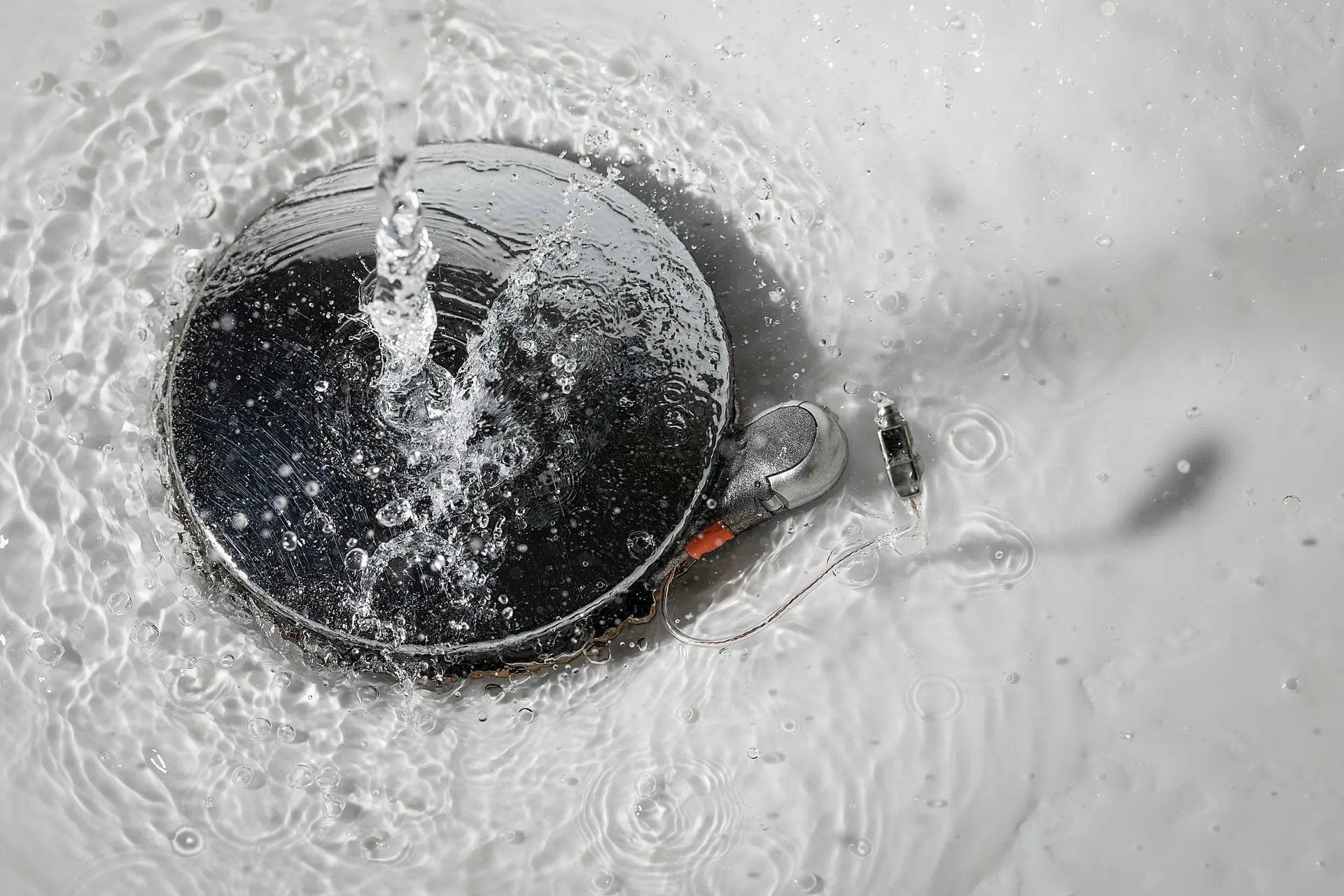 Hörgerät auf einem Gullydeckel, umspült von Wasser